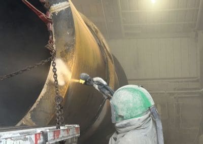 A blast media specialist spraying the outside of a large pipe