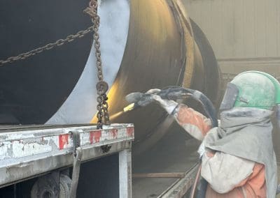 A blast media specialist spraying the outside of a large pipe