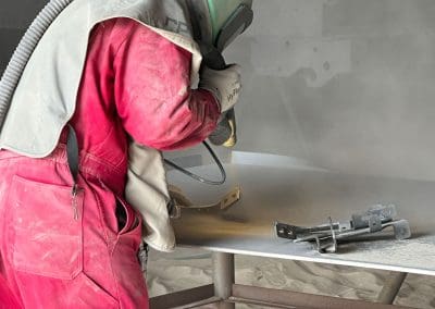 A blast media specialist spraying small individual metal part