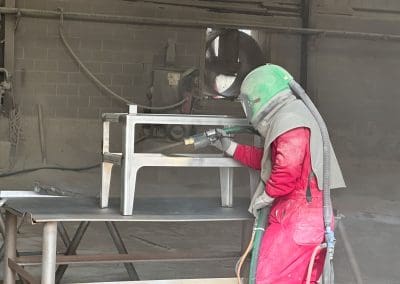 A blast media specialist sandblsting a metal table