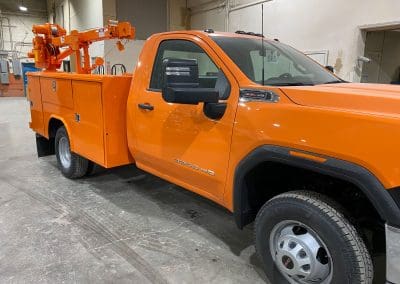 A specialized work pickup truck with a truck crane on the bed painted to match the fleet with a bright orange color