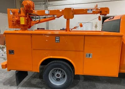 A specialized work truck with a truck crane painted to match the fleet with a bright orange color