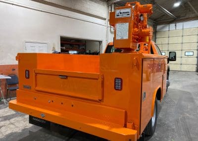 A specialized work truck with a truck crane painted to match the fleet with a bright orange color