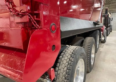 Custom paint job of a semi dump truck. Shows a duotone paint combination with high quality red paint and a protective bedliner coating on the side rail